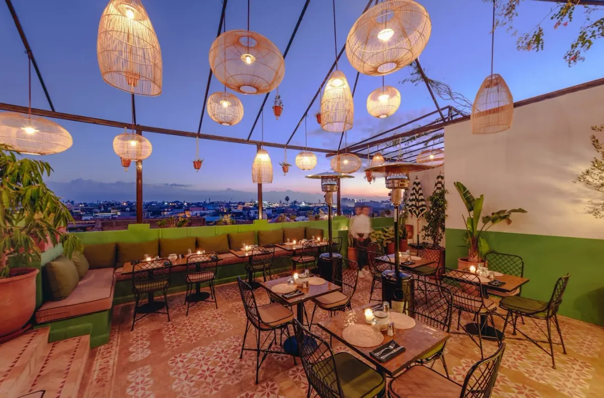 Rooftop de L'Mida à Marrakech au crépuscule : suspensions en rotin, banquettes vertes et vue sur les toits de la médina