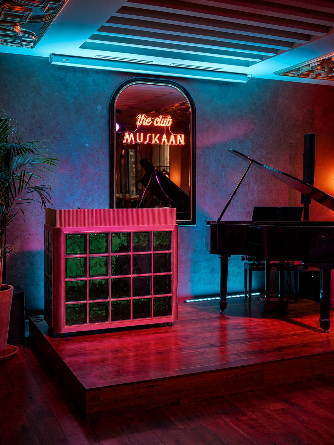 Scène du club Muskaan : enseigne néon, piano à queue et pupitre DJ