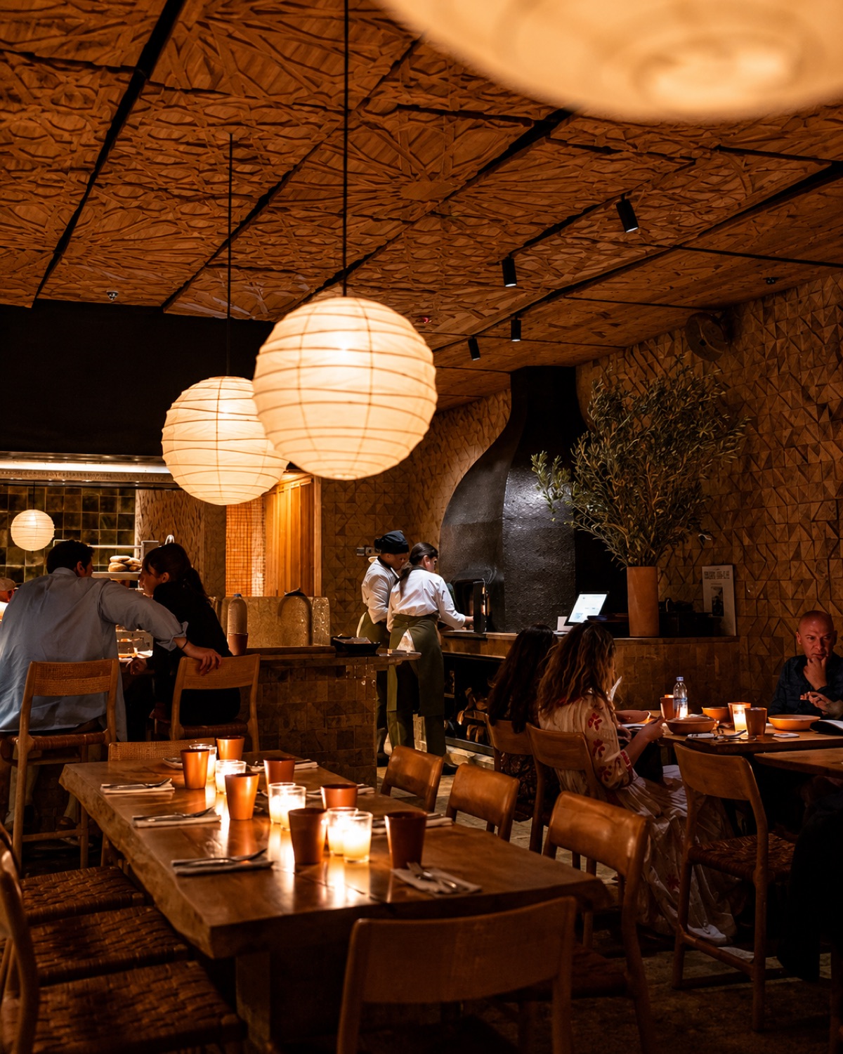 Grande salle de Sahbi Sahbi à Marrakech : plafond de bois sculpté, lanternes en papier et brigade féminine en cuisine ouverte