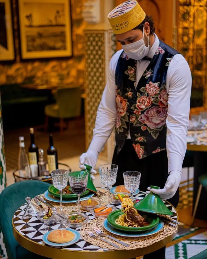 Serveur de Dar Dada en gilet fleuri présentant les tajines verts